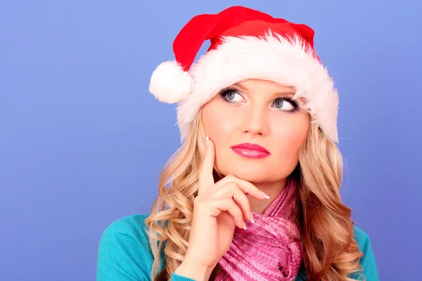 Красива різдвяна жінка думає в капелюсі Санти на синьому фоні — стокове фото