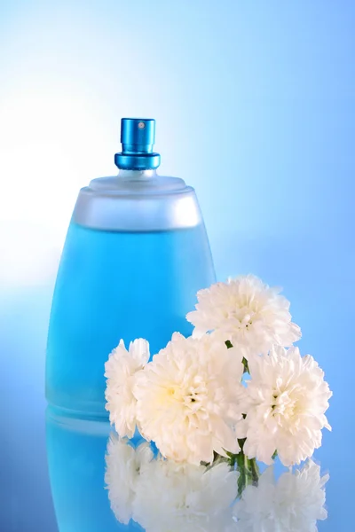 Parfüm şişesi ve mavi zemin üzerine çiçek — Stok fotoğraf