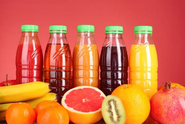 Flaskor juice med mogna frukter på röd bakgrund — Stockfoto