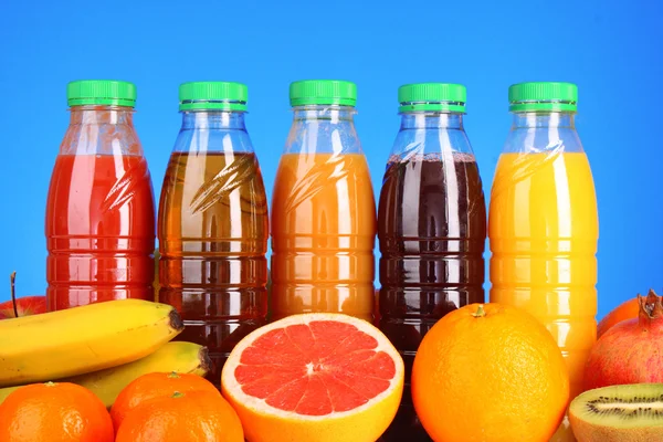 Bottles of juice with ripe fruits on blue background — Stock Photo, Image