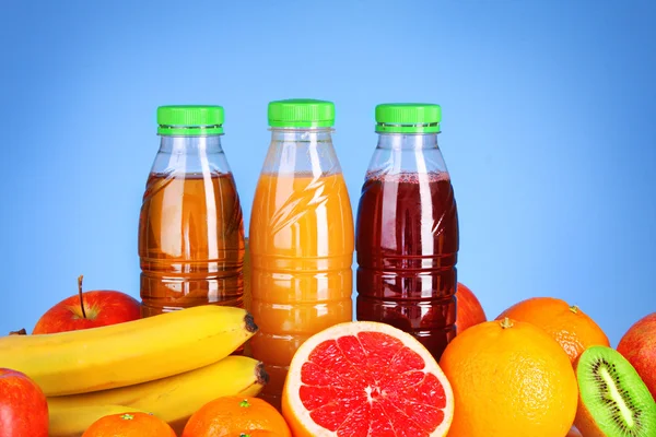 Бутылки сока с спелыми фруктами на голубом фоне — стоковое фото