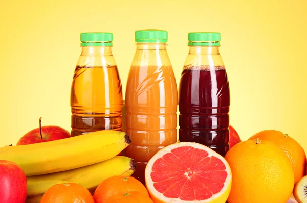 Frascos de jugo con frutas maduras sobre fondo amarillo — Foto de Stock