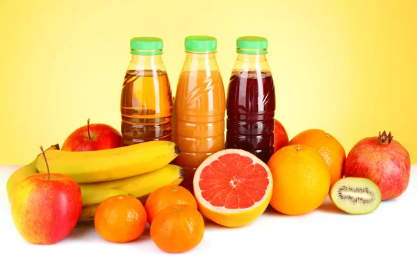 Garrafas de suco com frutas maduras no fundo amarelo — Fotografia de Stock