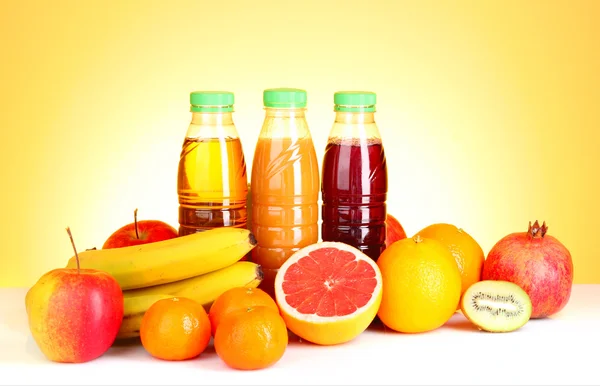 Бутылки сока с спелыми фруктами на желтом фоне — стоковое фото