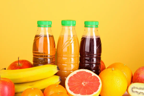 Frascos de jugo con frutas maduras sobre fondo amarillo —  Fotos de Stock