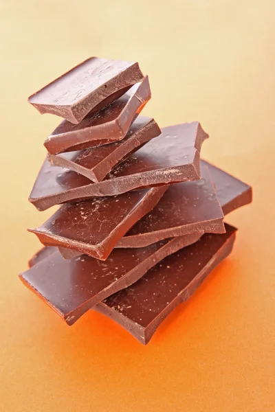 Stack Of Dark Chocolate Pieces, Over Orange Background — Stock Photo, Image