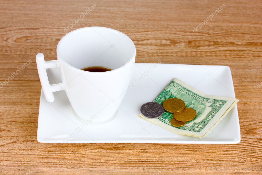 Empty cup of coffee with five dollars tip on wooden background.