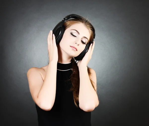Όμορφη νεαρή γυναίκα με ακουστικά σε σκούρο φόντο — Φωτογραφία Αρχείου
