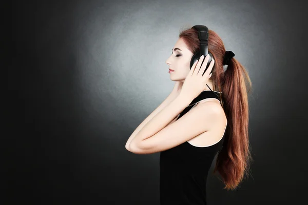 Beautiful young woman with headphones on dark background — Stock Photo, Image