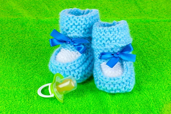Blue baby booties and pacifier on green background — Stock Photo, Image