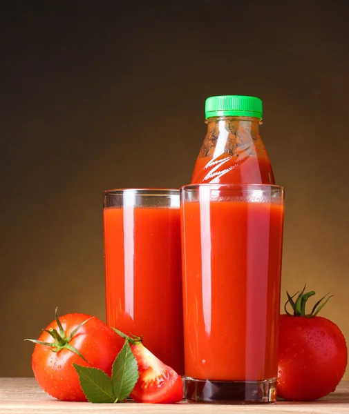 Jugo de tomate en vasos y tomate sobre mesa de madera sobre fondo marrón — Foto de Stock
