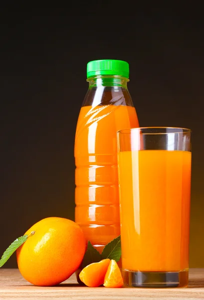 Tangerines, verre à jus et bouteille sur table en bois sur fond marron — Photo