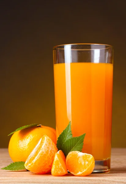 Tangerines and juice glass on wooden table on brown background — Stockfoto
