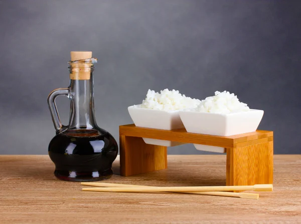 Tigelas de arroz cozido e molho de soja em jarra na mesa de madeira — Fotografia de Stock