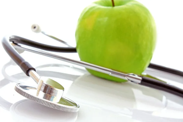 Stethoskop und grüner Apfel auf weißem Hintergrund — Stockfoto