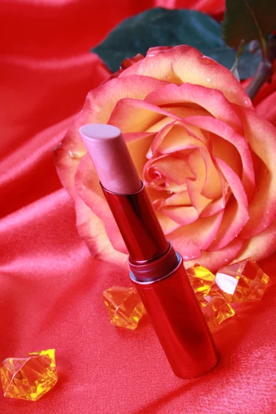 Lippenstift und Rose auf dem textilen Hintergrund Stockbild