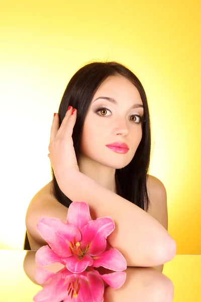 Beautiful young woman with lily flower on yellow background with — Stock Photo, Image