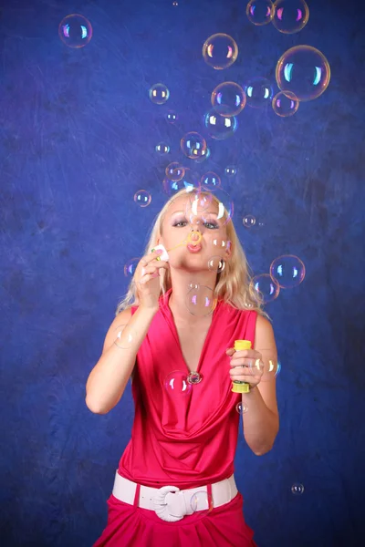 美丽的年轻女子在蓝色上吹肥皂泡泡 — 图库照片
