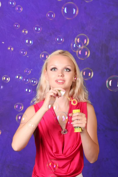 Beautiful young woman blowing soap bubbles on blue — Stock Photo, Image