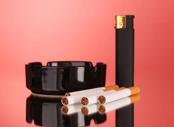 Cigarettes, cendrier et briquet sur fond rouge — Photo