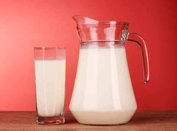 Кувшин и стакан с молоком на красном фоне — стоковое фото