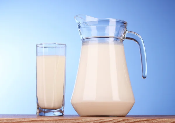 Tillbringare och glas med mjölk på blå bakgrund — Stockfoto
