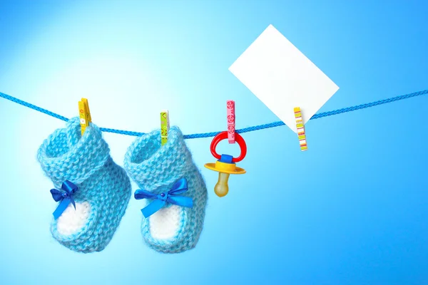 Botas de bebê, mamilo e cartão branco em um fundo azul — Fotografia de Stock