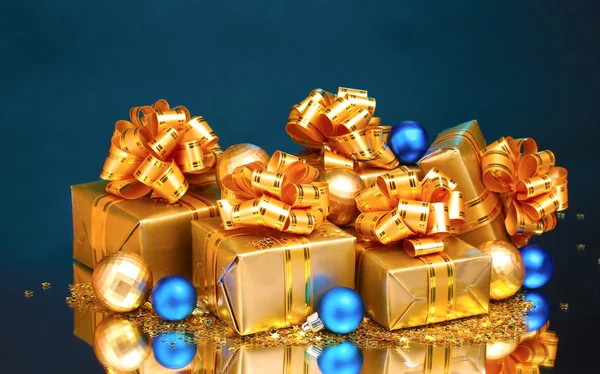 Gyönyörű ajándékokat az arany csomagolás és karácsonyi golyókat a kék ba — Stock Fotó