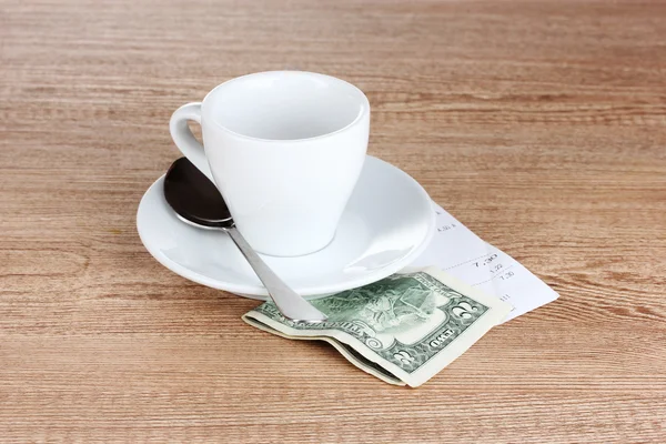 Empty cup of coffee with five dollars tip on wooden background — Stock Photo, Image