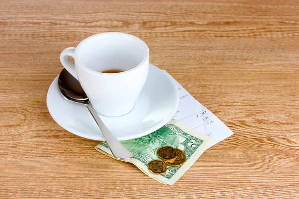 Empty cup of coffee with five dollars tip on wooden background — Stock Photo, Image