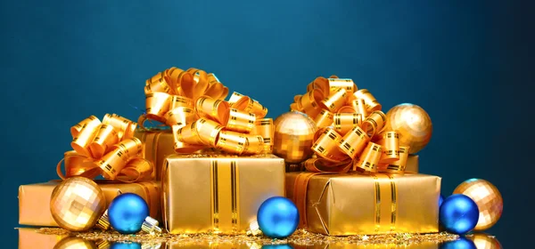 Schöne Geschenke in Goldverpackung und Weihnachtskugeln auf blauem Ba — Stockfoto