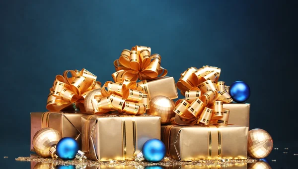 Beautiful gifts in gold packaging and Christmas balls on blue ba — Stock Photo, Image