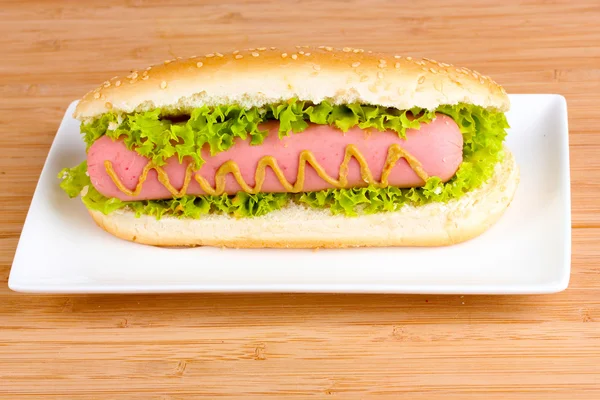Délicieux hot dog avec moutarde et laitue sur assiette sur ba en bois — Photo