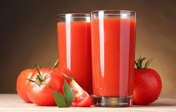 Tomato juice in glasses and tomato on wooden table on brown back — Stock Photo, Image