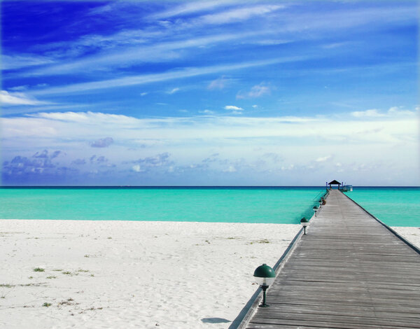 Wooden jetty on over the beautiful Maldivian beach with blue sky and clouds