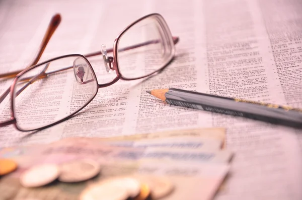 眼镜、 金钱和铅笔在报纸上 免版税图库图片