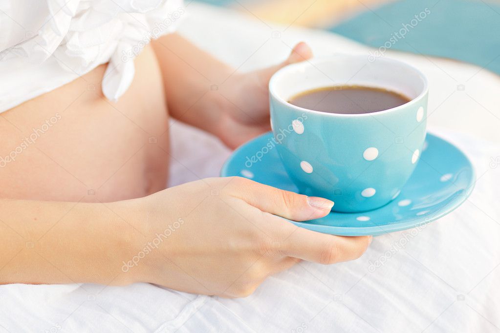 Beautiful pregnant belly with a cup in his hand, blue polka dots