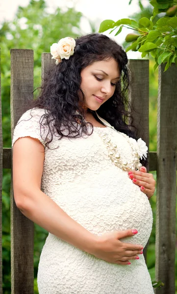 Linda garota grávida em um jardim perto da cerca — Fotografia de Stock