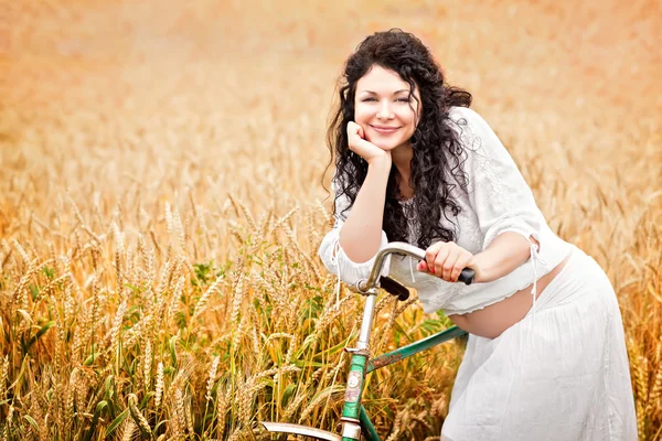 Милая беременная девушка с велосипедом в поле — стоковое фото