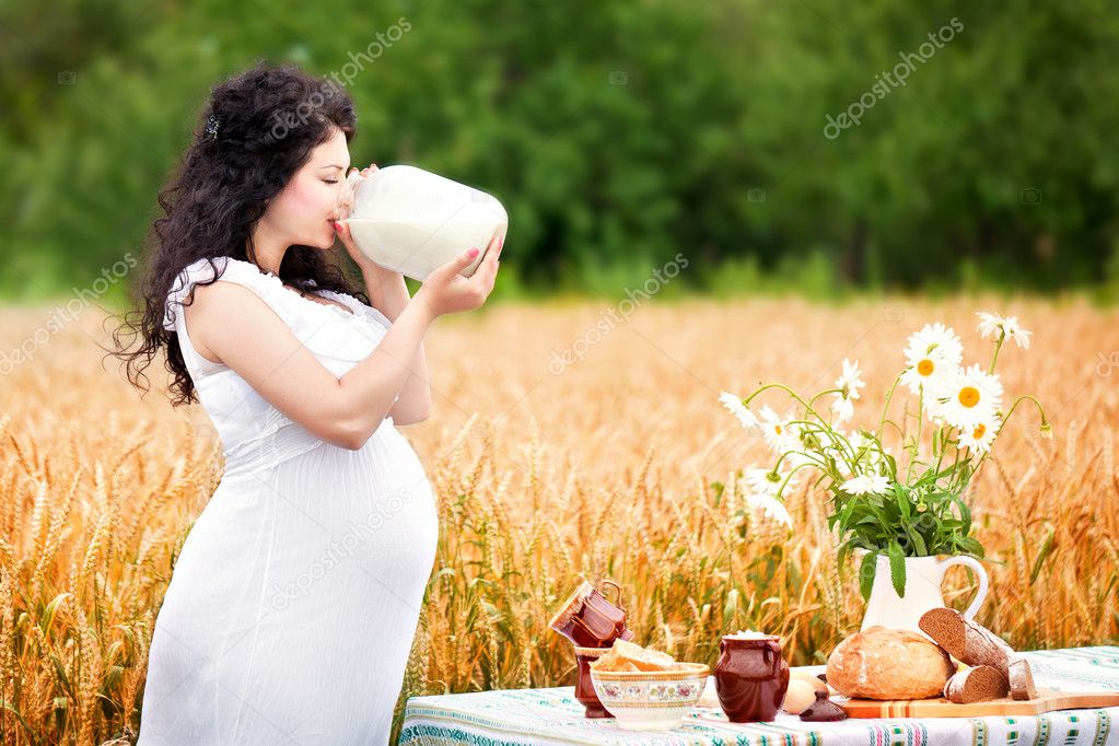 Cute pregnant girl drinks milk in a field