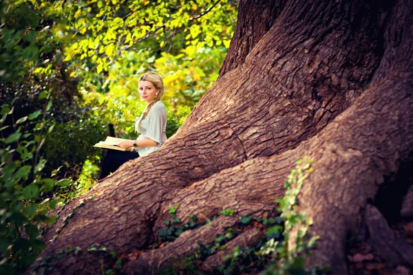 Cute dziewczyna w ciąży, czytanie na korzenie starych drzew — Zdjęcie stockowe