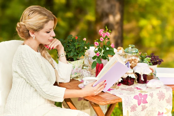 Мила дівчина в саду п'є чай і читає книгу — стокове фото