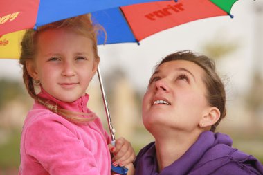 kız ve anne rengi şemsiyesi altında saklanıyorlar.