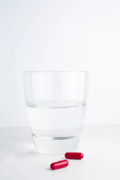 Yanında su bardağı Kırmızı hapları — Stok fotoğraf