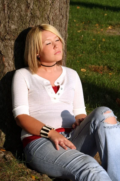 Blond Woman Sitting And Sunning Herself By Tree