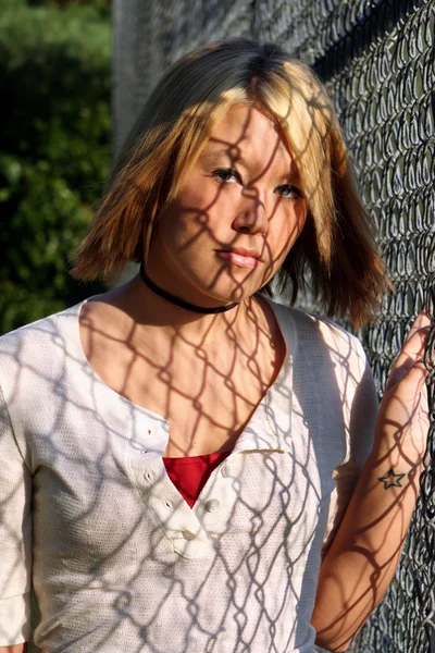 Junge blonde Frau mit Schatten am Zaun — Stockfoto