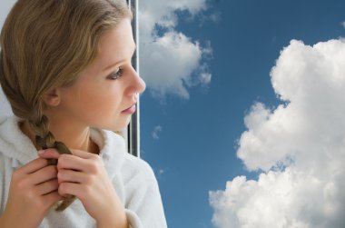 Beautiful young girl braids her hair by the window clipart