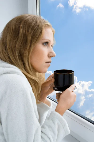 Jeune belle fille buvant du café par la fenêtre le matin — Photo