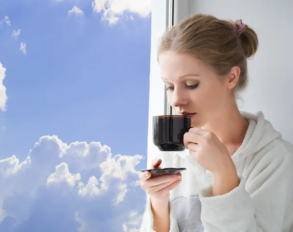 Молода красива жінка п'є каву біля вікна — стокове фото