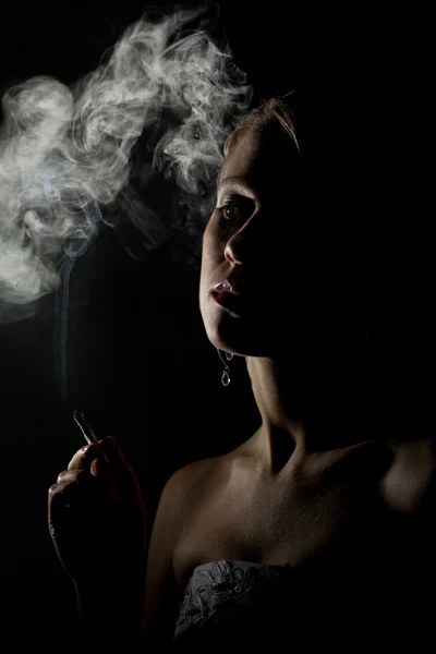 Krásná žena s cigaretou v temnotách — Stock fotografie